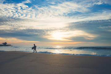 A man is alone a silent ocean coast in Portugal. He is going to meet waves on beautiful summer evening. Just him, his board and the ocean