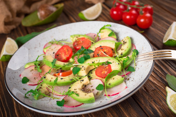 Vegetable salad with avocado, arugula, radish, lime and olive oil. Dietary healthy food. Wooden rustic background. Top view