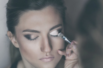 Obraz premium Young beautiful woman applying make-up by make-up artist. Process of making makeup.