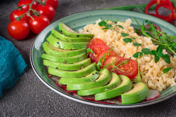 Porridge bulgur with salad avocado, tomatoes and arugula. Rustic concrete background. Top view