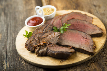 Sliced roast beef on the wooden cutting board with sauces