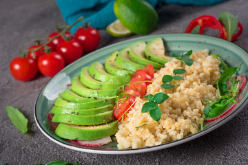 Porridge bulgur with salad avocado, tomatoes and arugula. Rustic concrete background. Top view