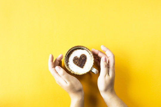 A female hand holds a cup of coffee on which a heart is drawn. Laik in social networks concept. Top view, flat lay