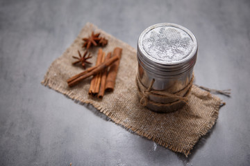 Cinnamon sticks and a jar of powdered sugar on a stone table.