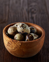 Fresh quail eggs in a wooden bowl on a dark wooden background, top view, close-up