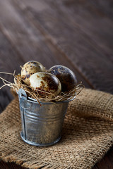 Small decorative bucket filled with quail eggs on homespun napkin over dark wooden table, close-up, selective focus.