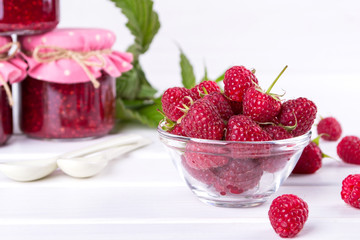 Red fresh raspberries in a glass bowl with green leaves on white background.