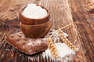 Wheat flour and bread in wooden bowl.