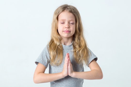 Little girl with her eyes closed folded her hands in prayer or meditation.