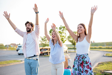 Fototapeta premium Group of friends hitchhiking on a side of the road. Jumping and waving to grab attention.