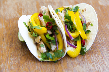 Tasty tacos with grilled chicken fillet, fresh vegetables, lime on rustic wooden background. Mexican kitchen. Side view, closeup.