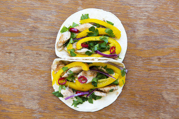 Tasty corn tortillas with fresh vegetables, grilled chicken fillet on rustic wooden background. Top view, from above.