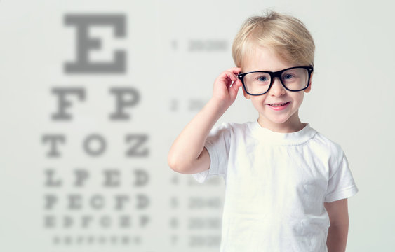 Little boy in glasses having eye test, over eye chart. Tables vision testing. Visiting a doctor pediatric ophthalmologist.