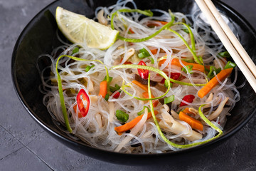 Vietnamese Pho Noodle Soup. Chilli, Rice Noodles, Bean Shoots showing noodles picked up with Chopsticks on a black background.