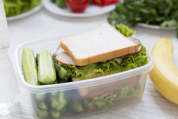 School lunch box with sandwich, fruits and bottle of water on white wooden background. Closeup.