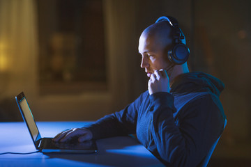 cybercrime, hacking and technology concept - male hacker with headset using laptop computer for...