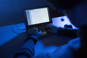 cybercrime, hacking and technology concept - hands of hacker in dark room writing code or using...