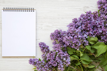 A bouquet of lilac flowers with notebook on a white wooden background. Mothers Day. Copy space. From above, flat lay.