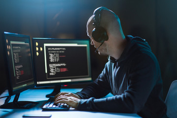 cybercrime, hacking and technology concept - male hacker with headphones and coding on laptop...