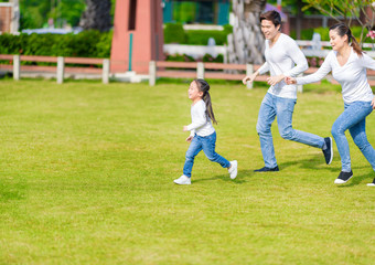 Obraz premium Little girl is running with parents in the park. Young family with little kid having fun in nature.