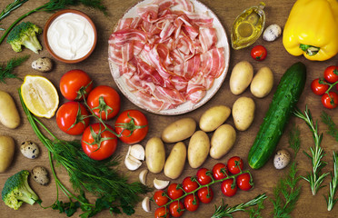 Countless summer vegetables, quail eggs and ham on the wooden rustic table. Concept of village menu, organic food.  
