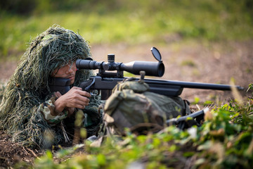 Sniper laying on the grass looking through scope at the target in deep forest.t.