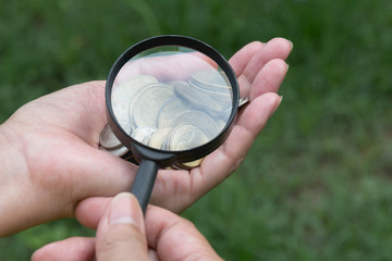 Male using magnifying glass look at the coins on hand for accounting and financial concept.