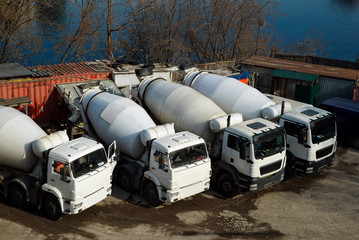 Concrete mixers trucks and construction materials on the parking near the river