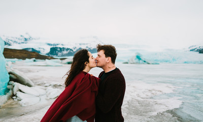 Iceland Wedding. Beautiful newlyweds kissing in Glacier Lagoon in cold windy day