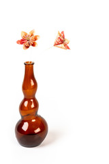 Two orange origami flowers in dark glass bottle on white background.