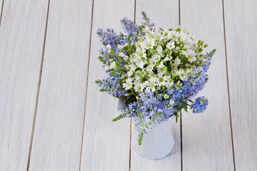 Bouquet of white and blue wild flowers in a cup on a wooden table
