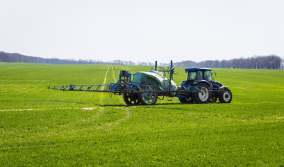 Tractor spraying insecticide to the green field, agricultural natural seasonal spring background