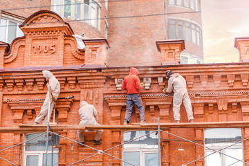 Unrecognizable workers in protective clothing are engaged in the restoration of the old brick...