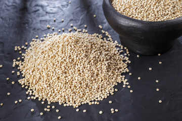 Quinoa grains with spoon and bowl on black background