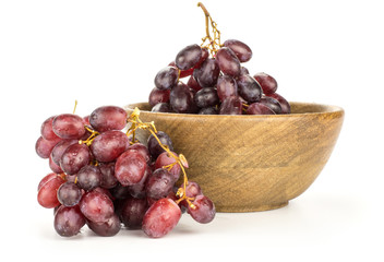 Red globe grape cluster in a wooden bowl isolated on white background shiny dark pink berries.