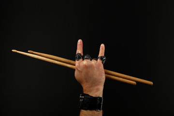 Man hand with drumsticks and devil horns on black