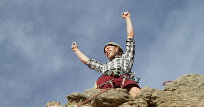 Climber cheering after reaching the top of cliff 