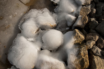 The frozen stones on the coast of the lake. Melting ice on the rocky beach.