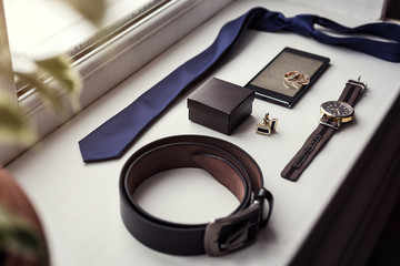 Different men's accessories such as: cufflinks, watches,  rings, belt, tie and phone - are on the table