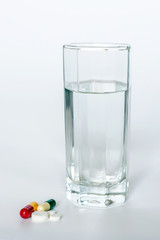 Glass of Water and Pills on white background. Concept of healthcare, illness and treatment.