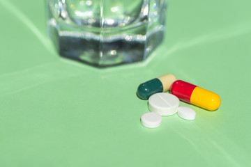 Glass of Water and Pills on green background. Concept of healthcare, illness and treatment.