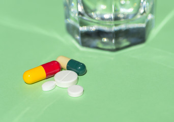 Glass of Water and Pills on green background. Concept of healthcare, illness and treatment.