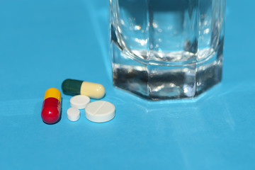 Pills and Glass of Water on blue background. Concept of healthcare, illness and disease treatment.
