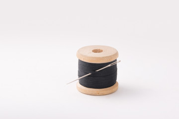 A wooden coil with threads of black color. The needle is threaded.