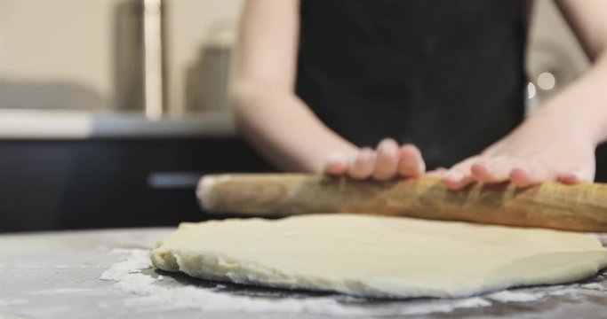 Close-up of children's hands roll out dough for pie in the kitchen.