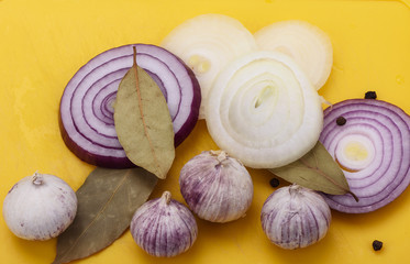 Onion, garlic, bay leaf with pepper on a yellow cutting board