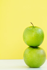 one green Apple on another on yellow background