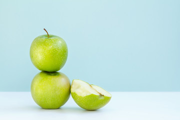 one green Apple on another and next half bitten Apple on blue background