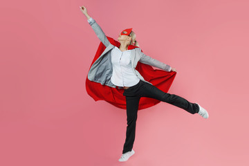 Young attractive woman superhero. Girl in a business suit and a mask with red cloak of hero.