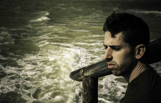 Retrato de hombre joven sentado en el muelle de madera al lado del mar